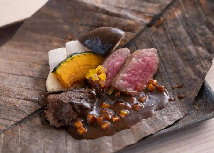 A serving of wagyu beef, vegetables and sauce on a large leaf, serving as a plate.